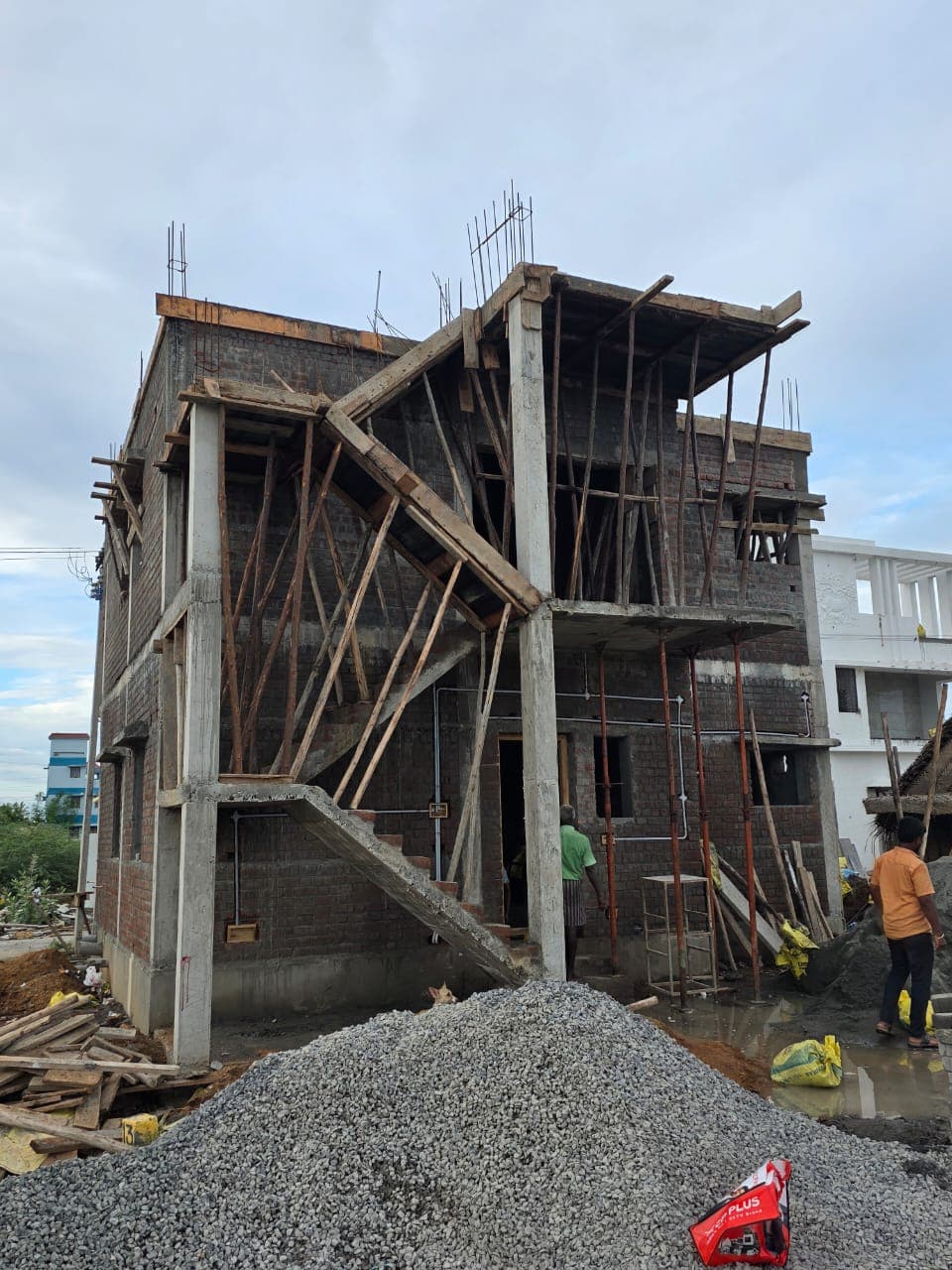 RCC frame of the Deeran Nagar residence rising through three floors with timber shuttering and a heap of graded aggregate.