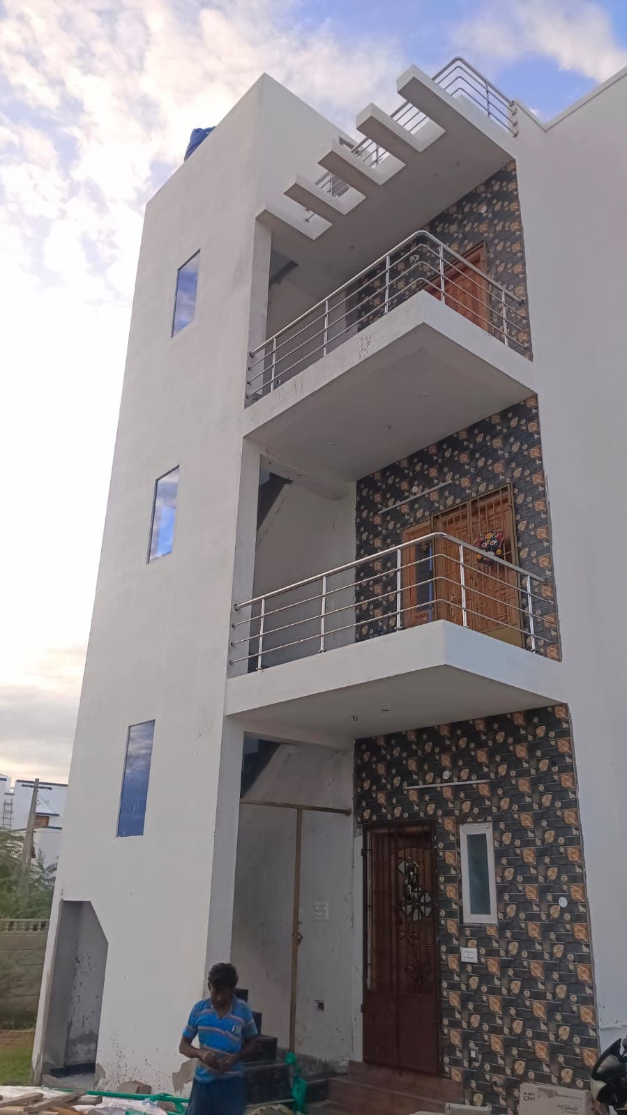 Completed three-storey residence at Deeran Nagar with white rendered facade, cantilevered balconies, and blue window accents.