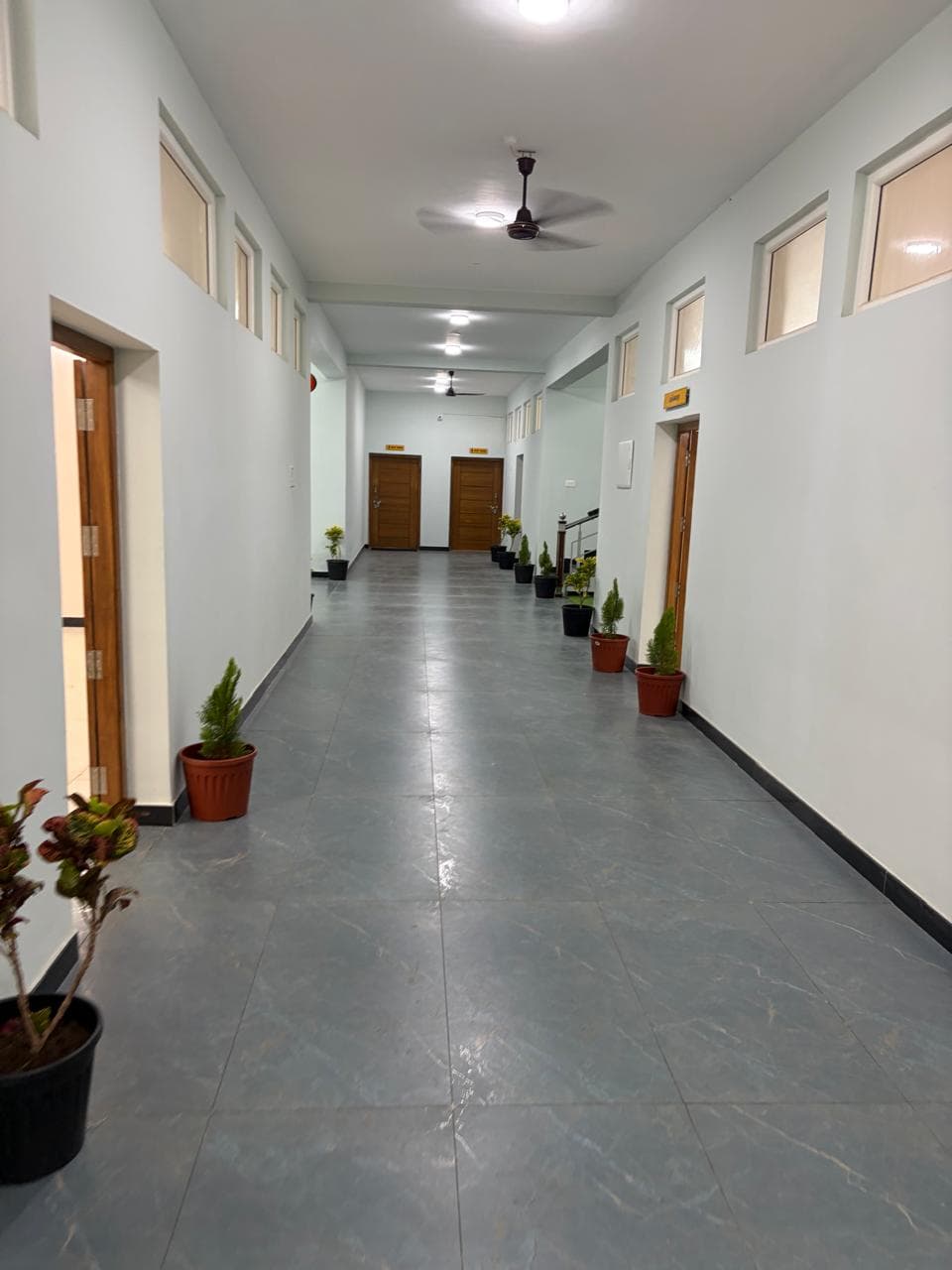 Long office corridor with polished granite flooring, panelled doors, and ceiling fans.