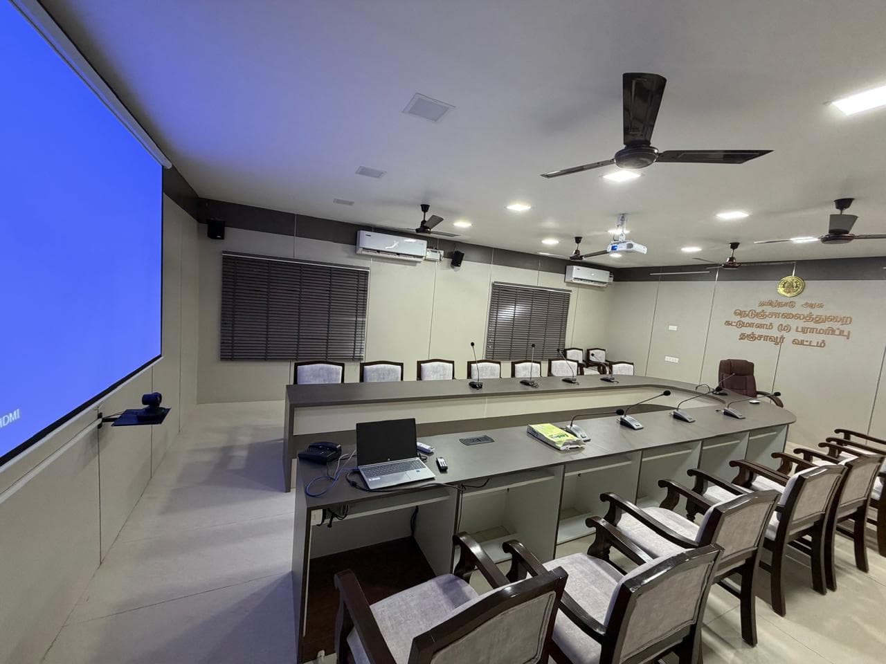 Meeting room fitted with a projection screen, panelled front wall, and rows of timber-framed seating.