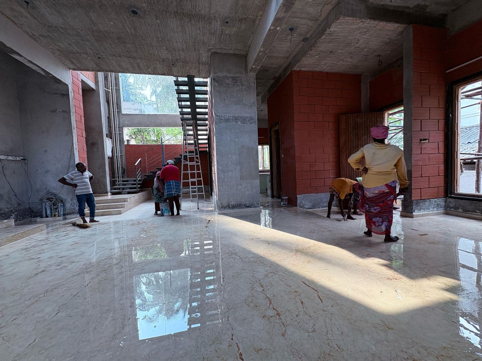 Polished marble hall during finishing works with the open staircase and brick-lined walls beyond.