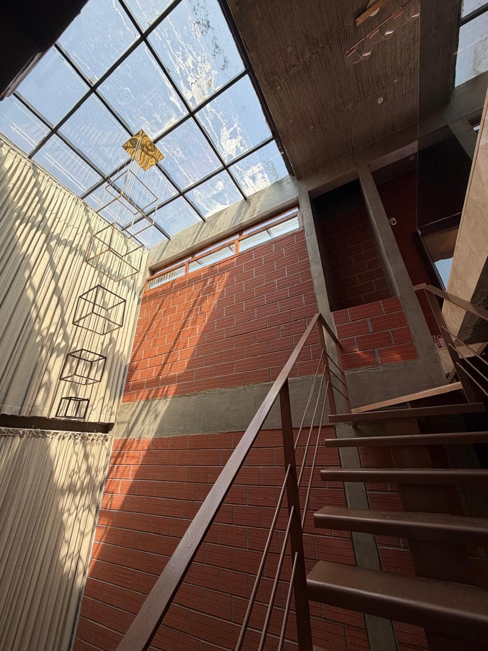 Skylit stairwell with a steel-framed glass roof throwing daylight across exposed brickwork.