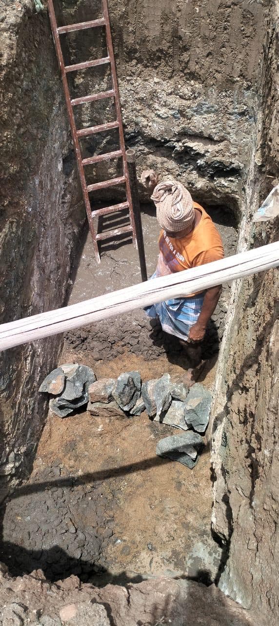 A worker standing in a deep foundation excavation cut through rock strata, with a ladder set against the face.